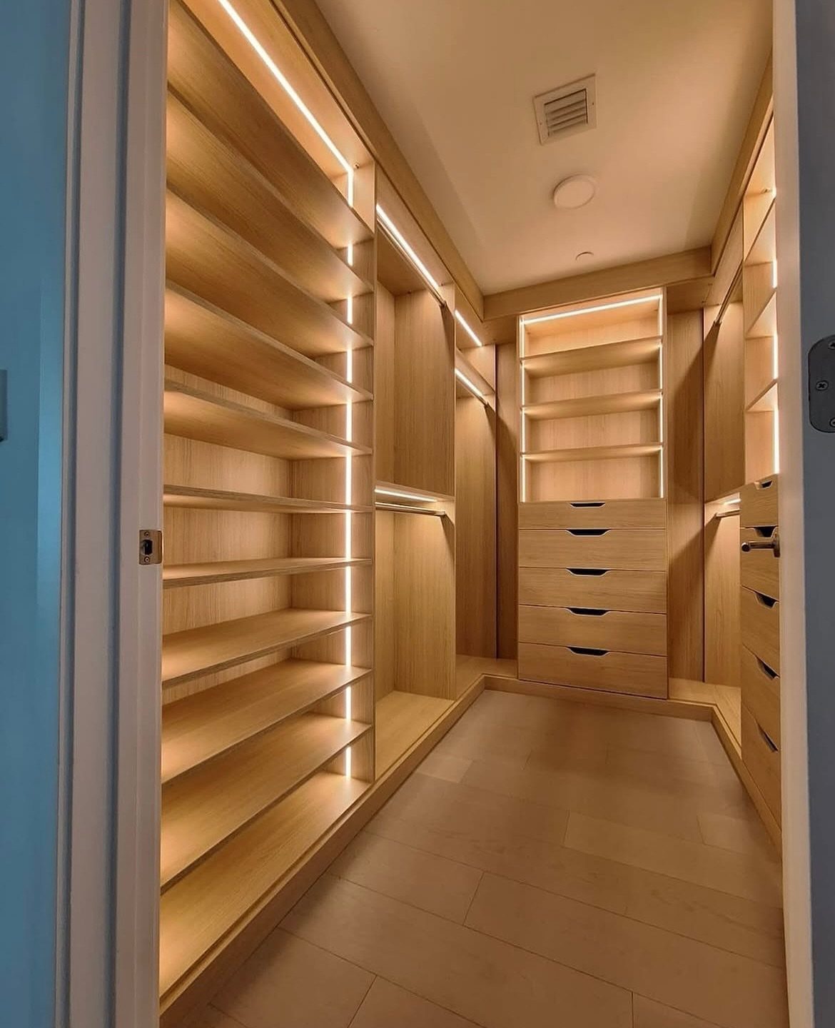 Walk-in closet with light wood shelving and integrated vertical LED strip lighting.