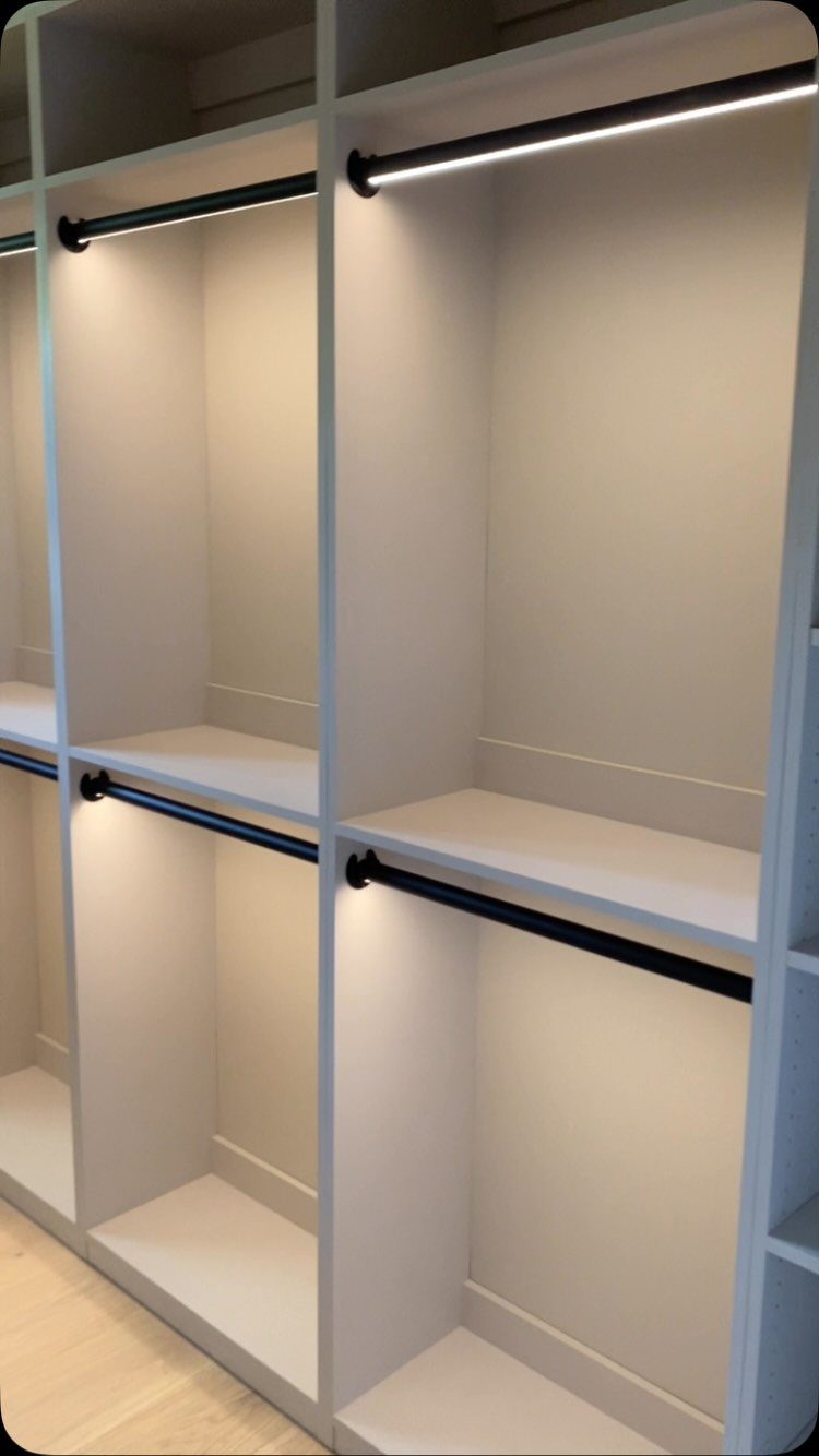 Lighted closet rods illuminating empty white shelving units in a modern walk-in closet.