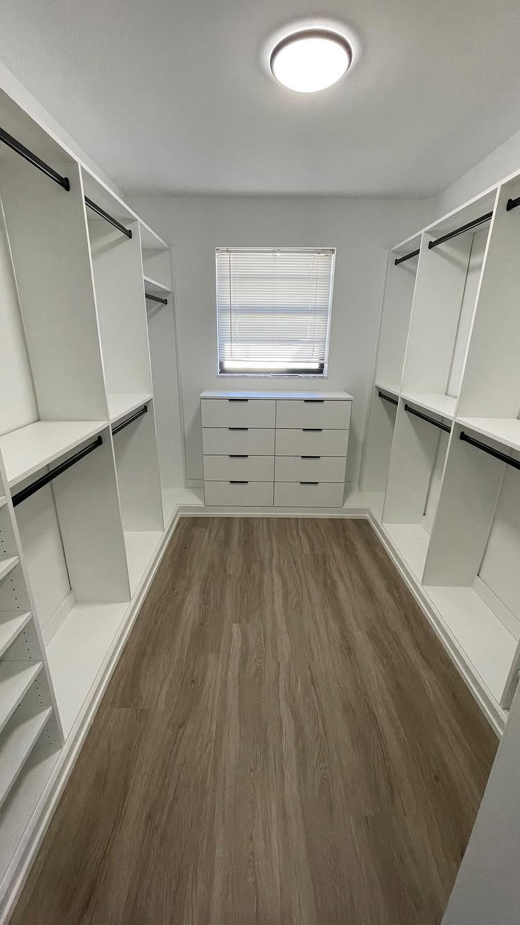 Walk-in closet with white shelving, wood floors, and a window providing natural light.
