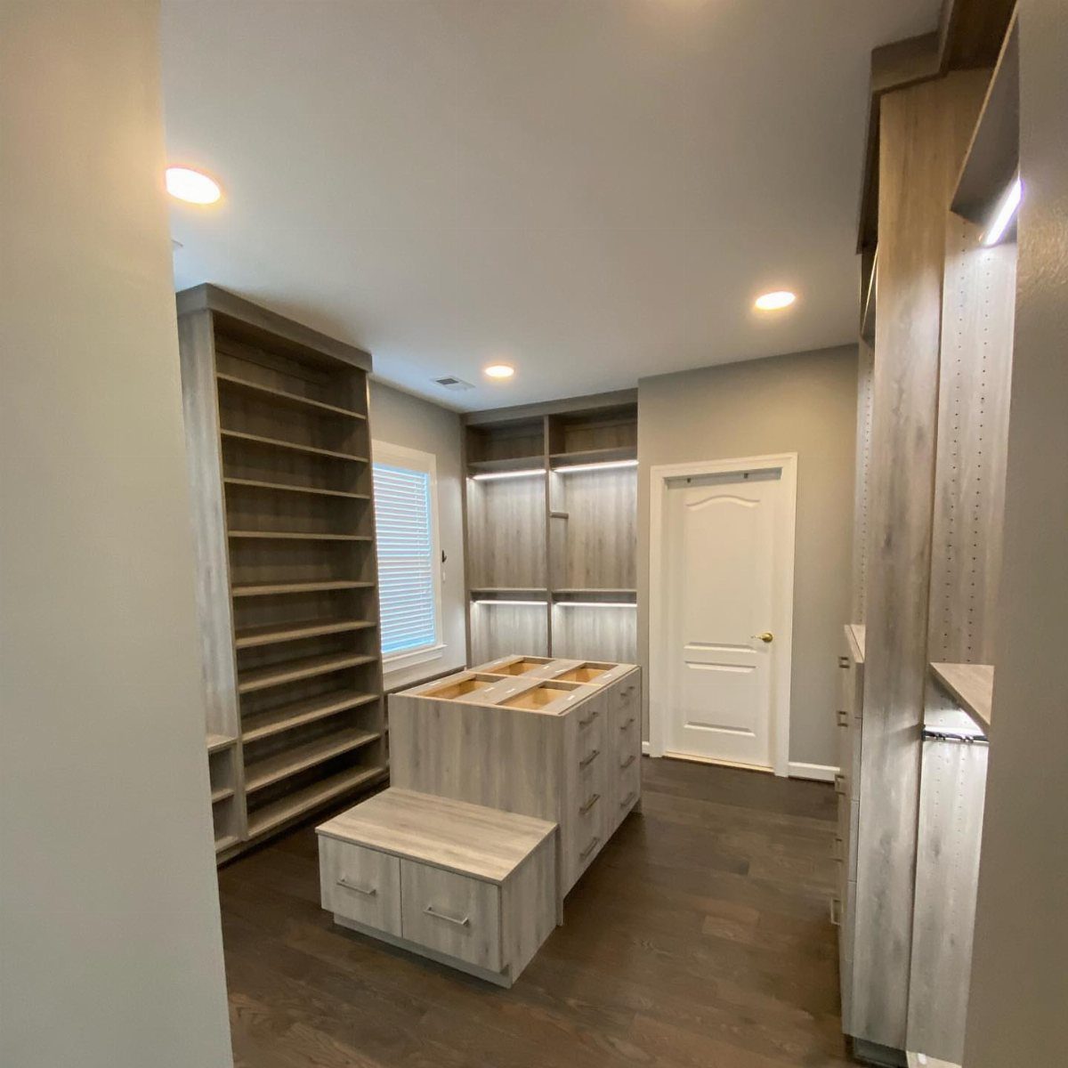 Modern walk-in closet with grey cabinetry, central island, and integrated vertical LED lighting.
