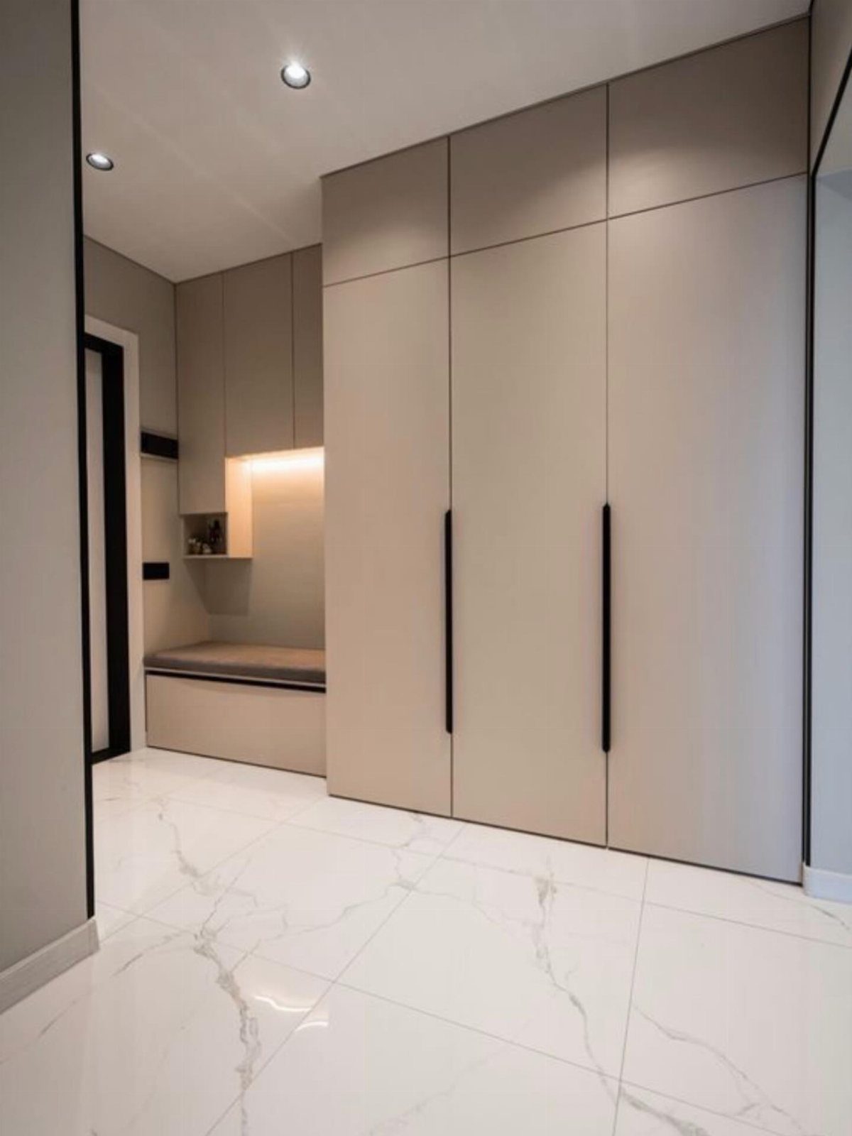 Built-in bench with grey cushion next to beige wardrobes in a modern closet.