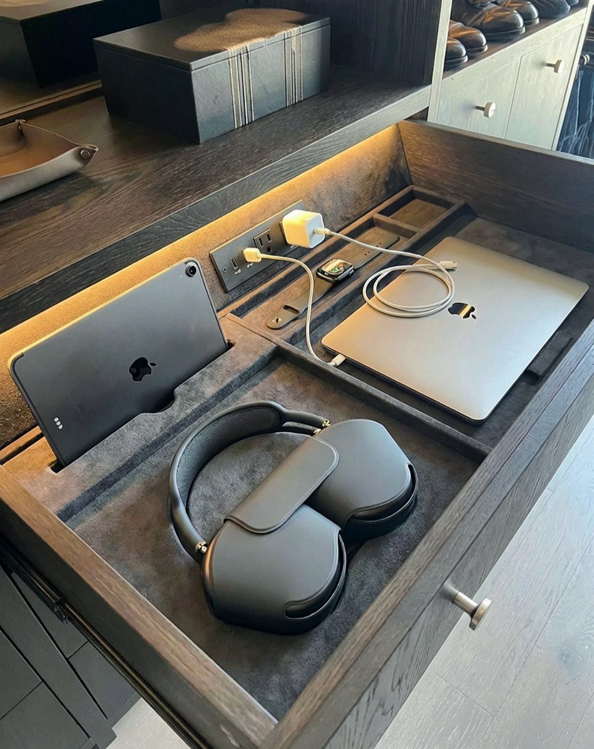 Open dark wood drawer with built-in power outlet charging a laptop and tablet.
