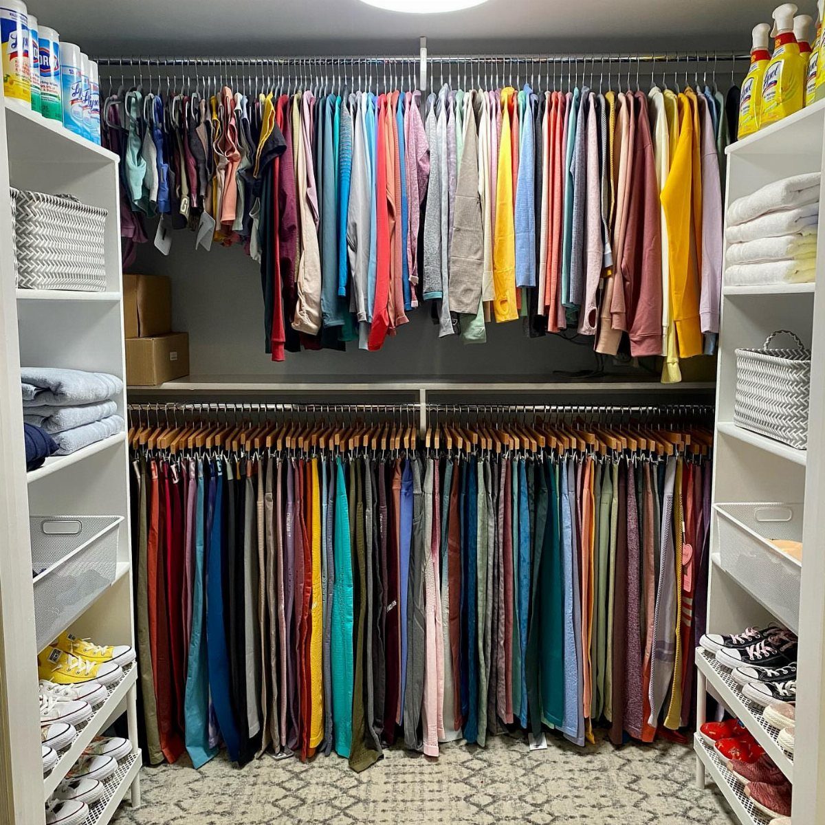 Color-coordinated clothing hanging in a walk-in closet with white shelving and patterned rug.