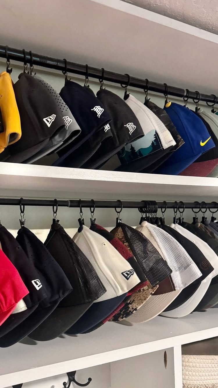 Baseball caps hanging from hooks on white closet shelves in an organized row.