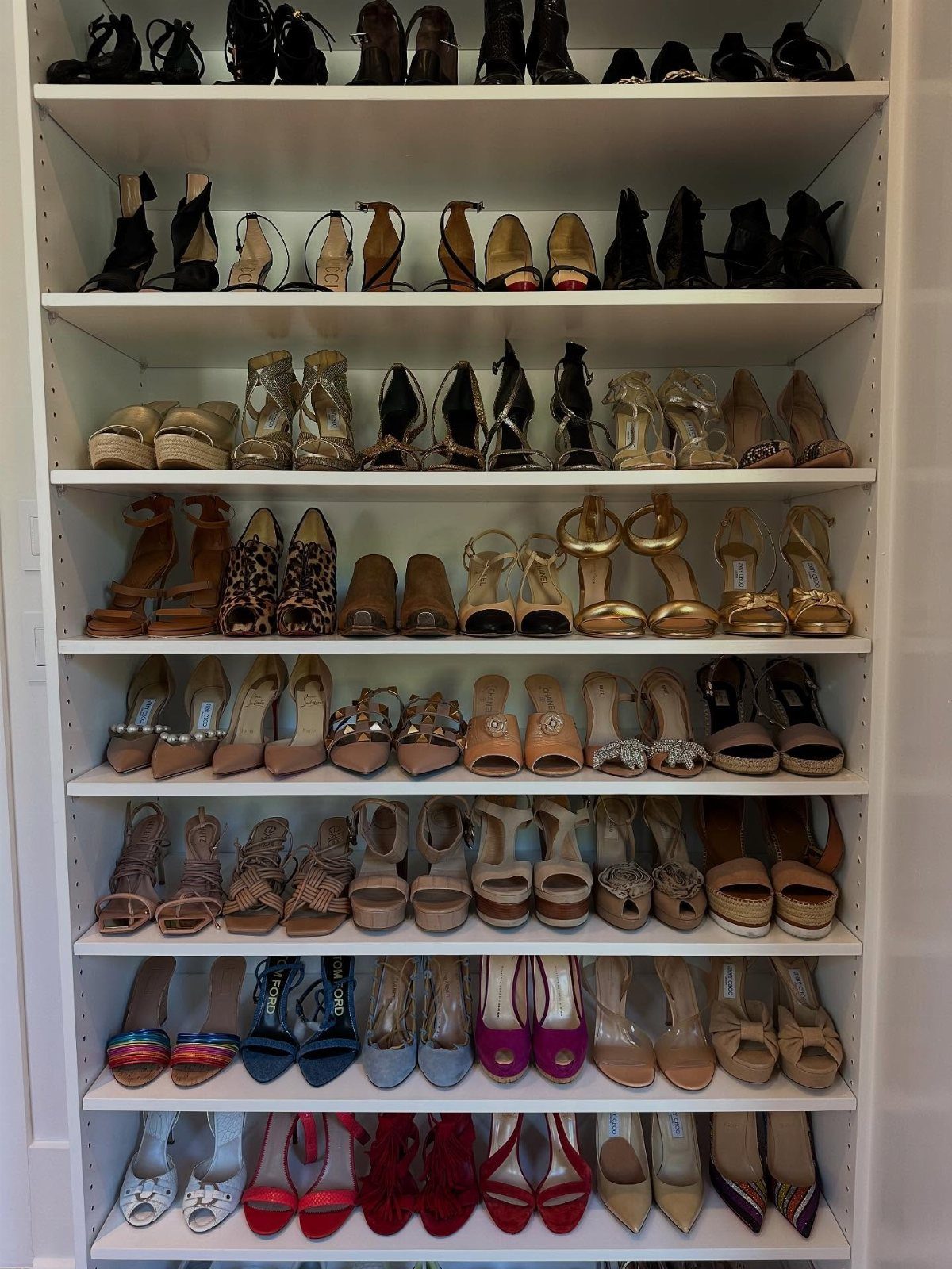 White built-in shoe shelves filled with organized rows of women's high heels and sandals.