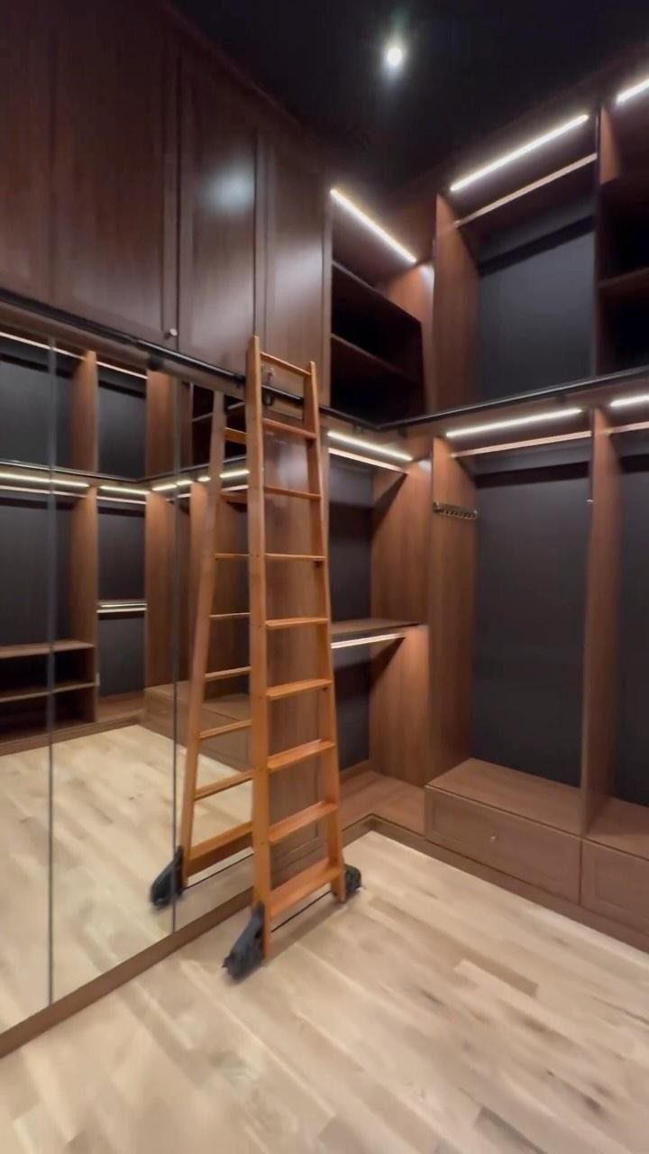 Dark wood walk-in closet with a rolling ladder and large mirrored sliding doors.