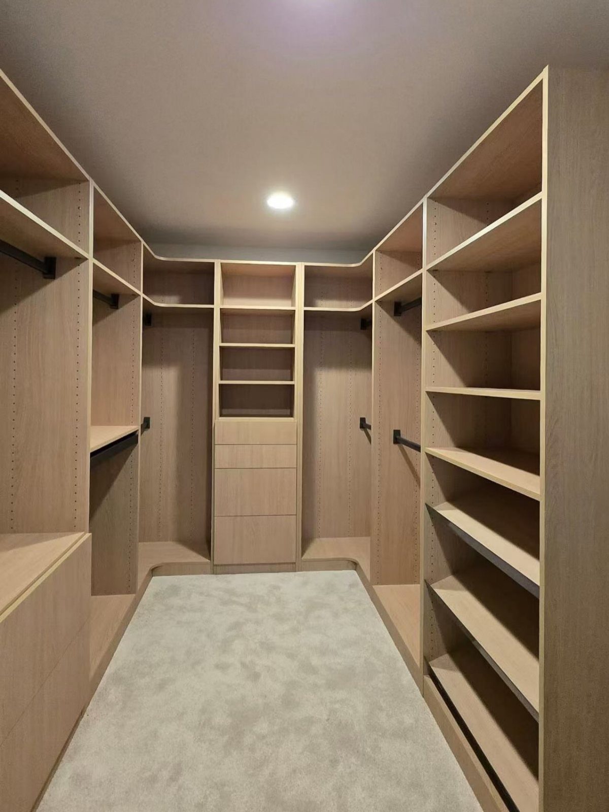 U-shaped walk-in closet with light wood shelving, hanging rods, and grey carpeting.