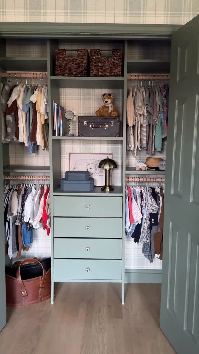 Child's built-in closet with sage green cabinetry and light plaid wallpaper backings.