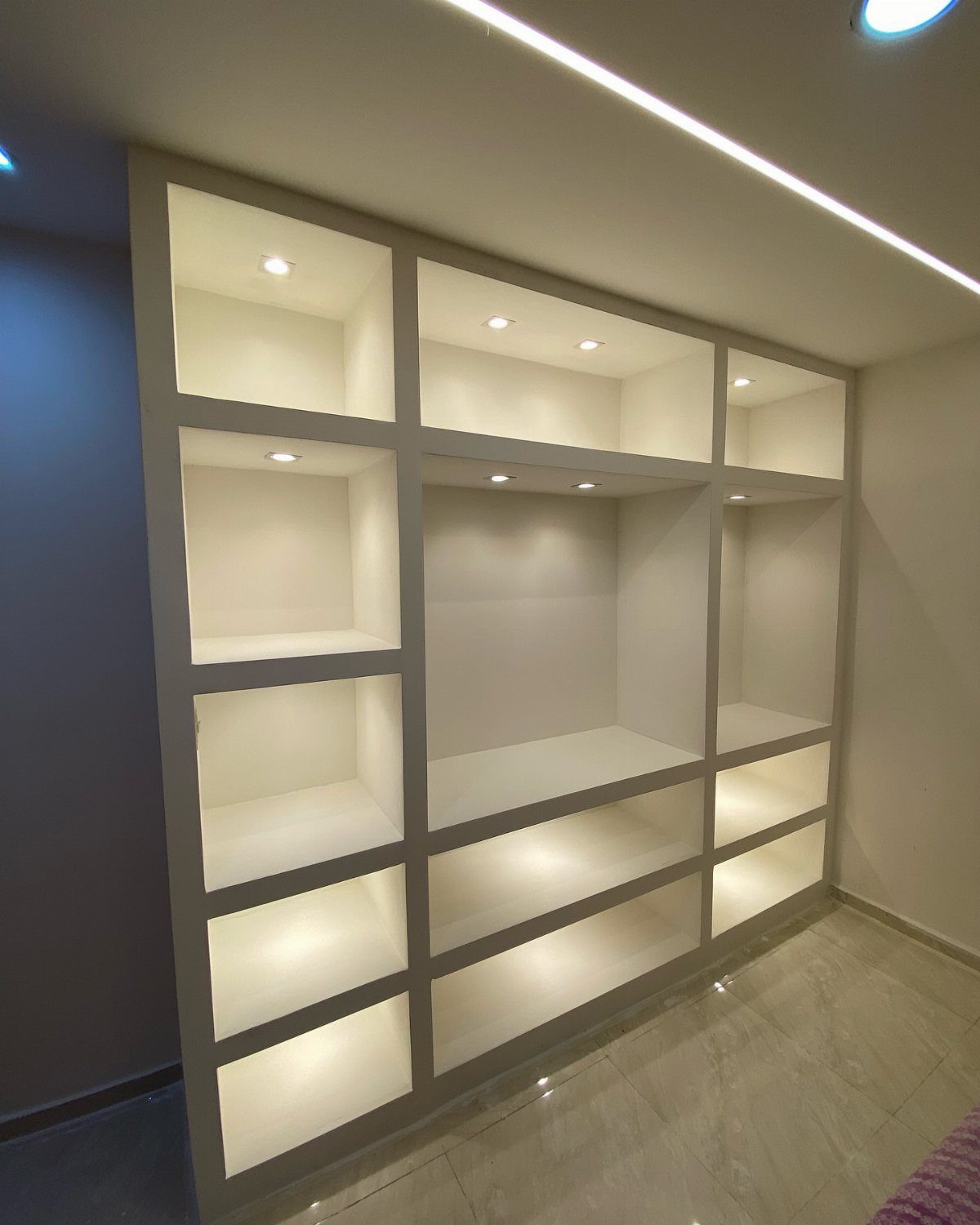 White built-in shelving unit with recessed accent lights illuminating the open compartments.