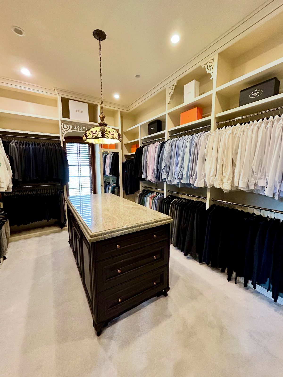 Spacious walk-in closet with white shelving, hanging clothes, and a central marble island.