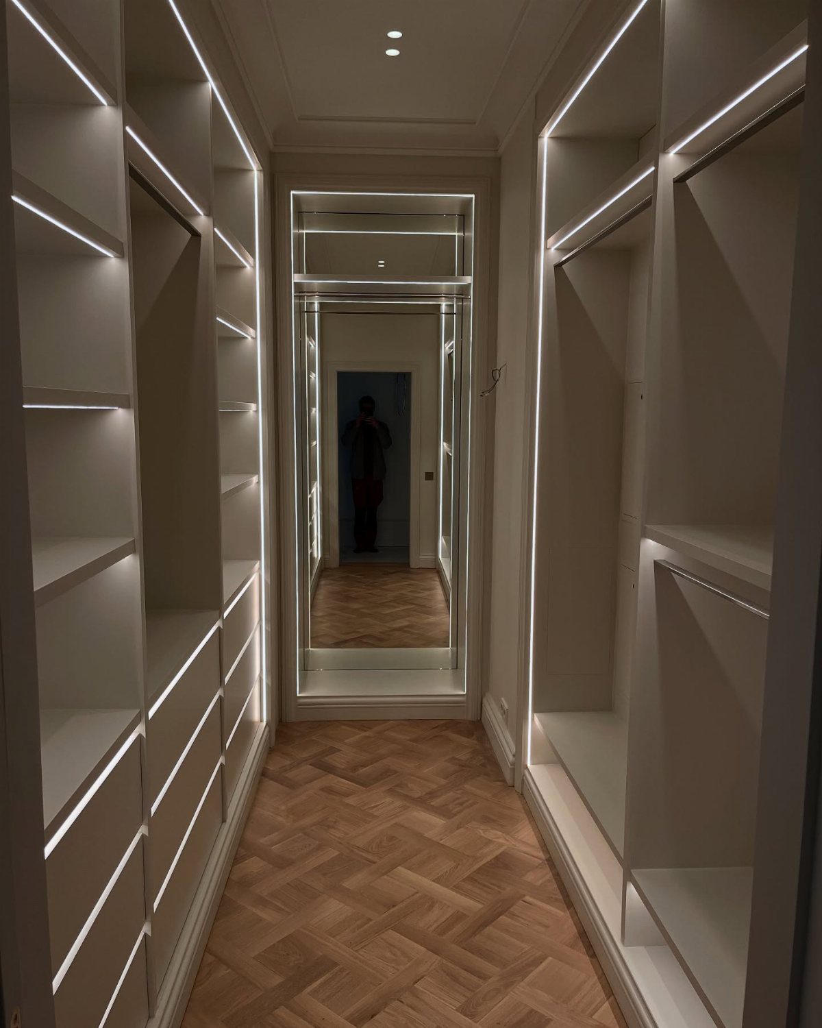 White walk-in closet with integrated LED strip lighting and herringbone wood floors.