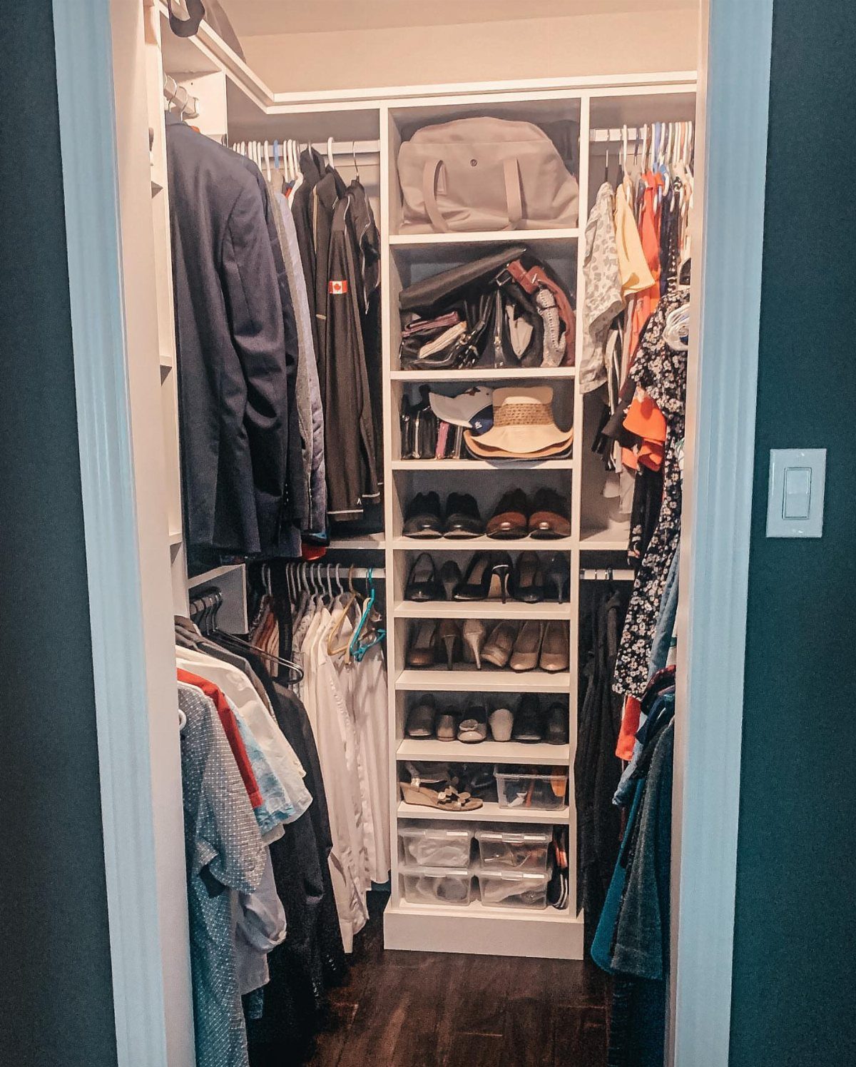 Narrow walk-in closet with white shelving, hanging clothes, and organized shoe storage.
