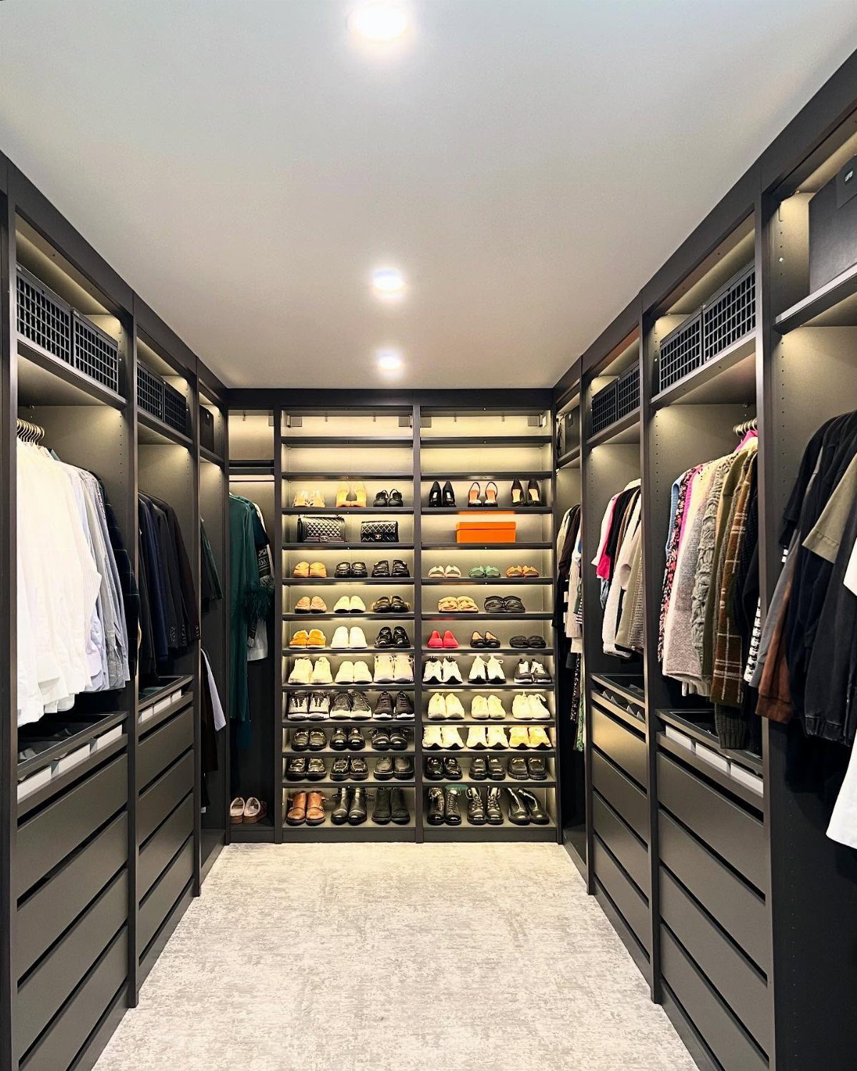 Modern walk-in closet with a central carpeted walkway and dark grey shelving.