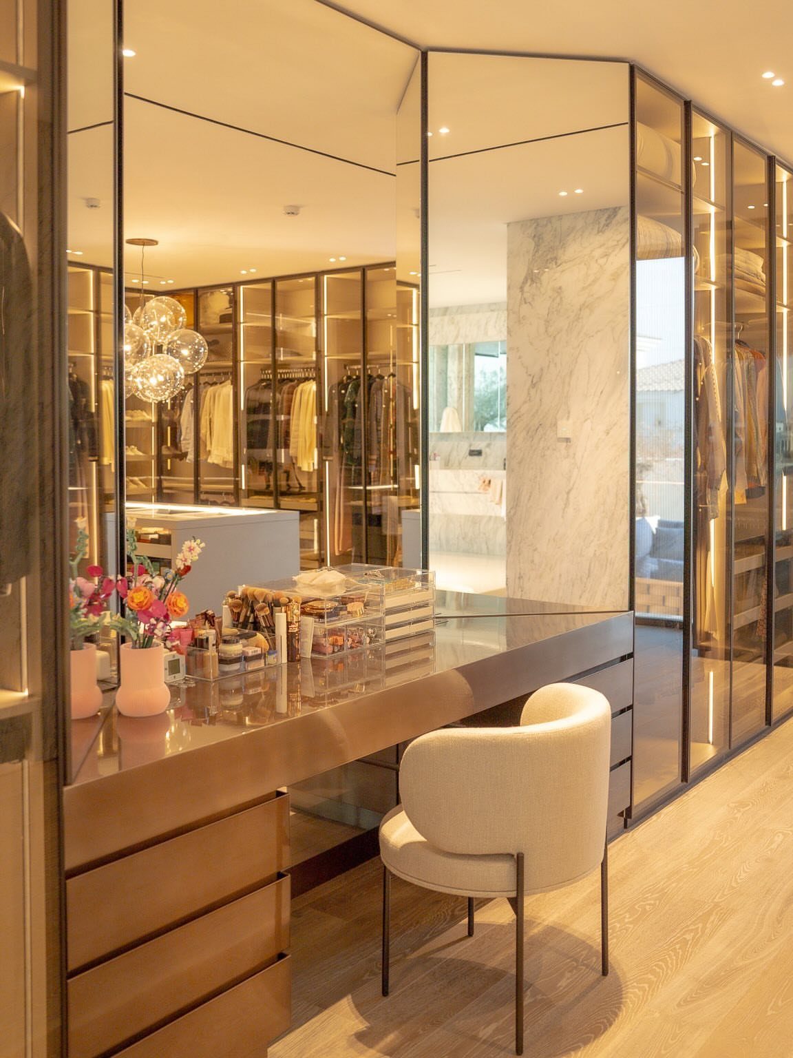 Luxurious walk-in closet with a vanity mirror and glass-fronted wardrobe storage systems.
