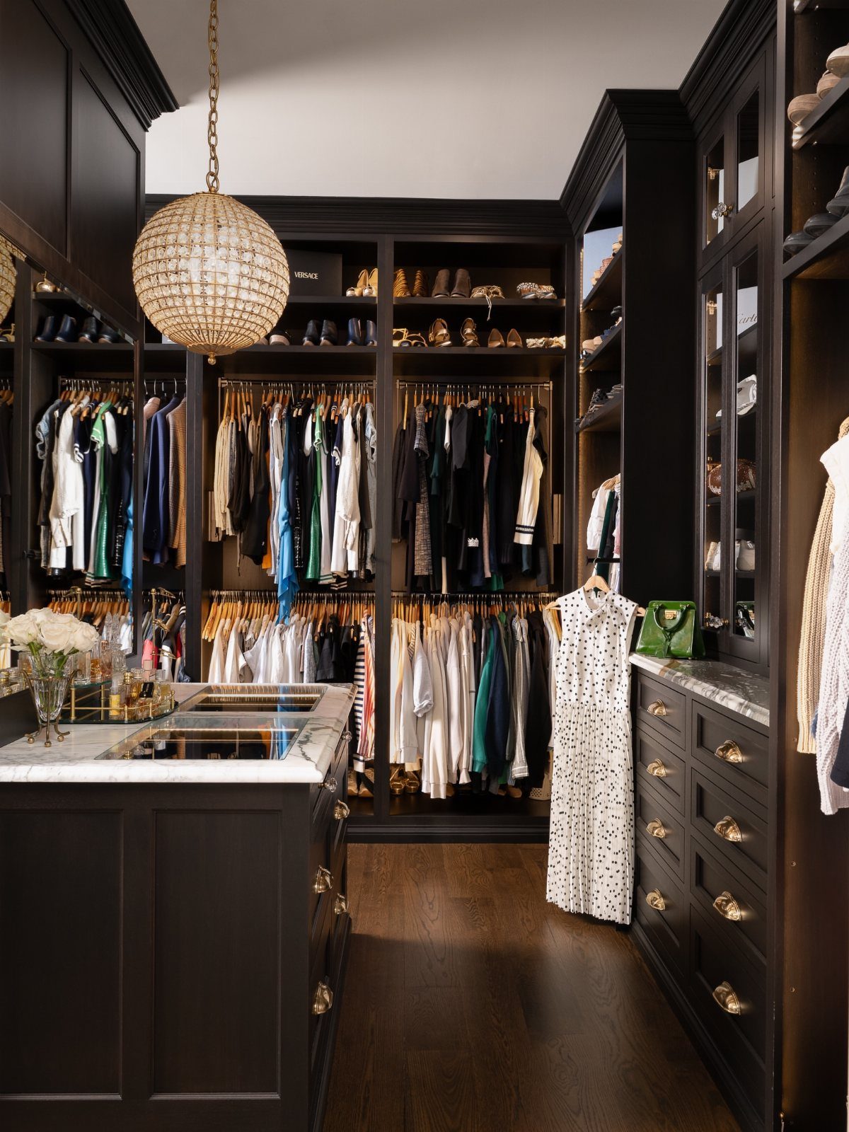 Luxurious walk-in closet with black cabinetry, organized clothing zones, and crystal chandelier.