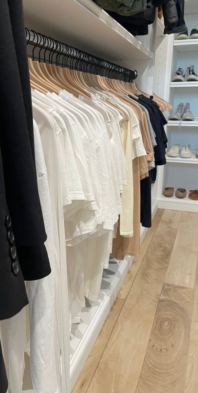 Wooden hangers holding a row of neutral colored clothes in a white closet.