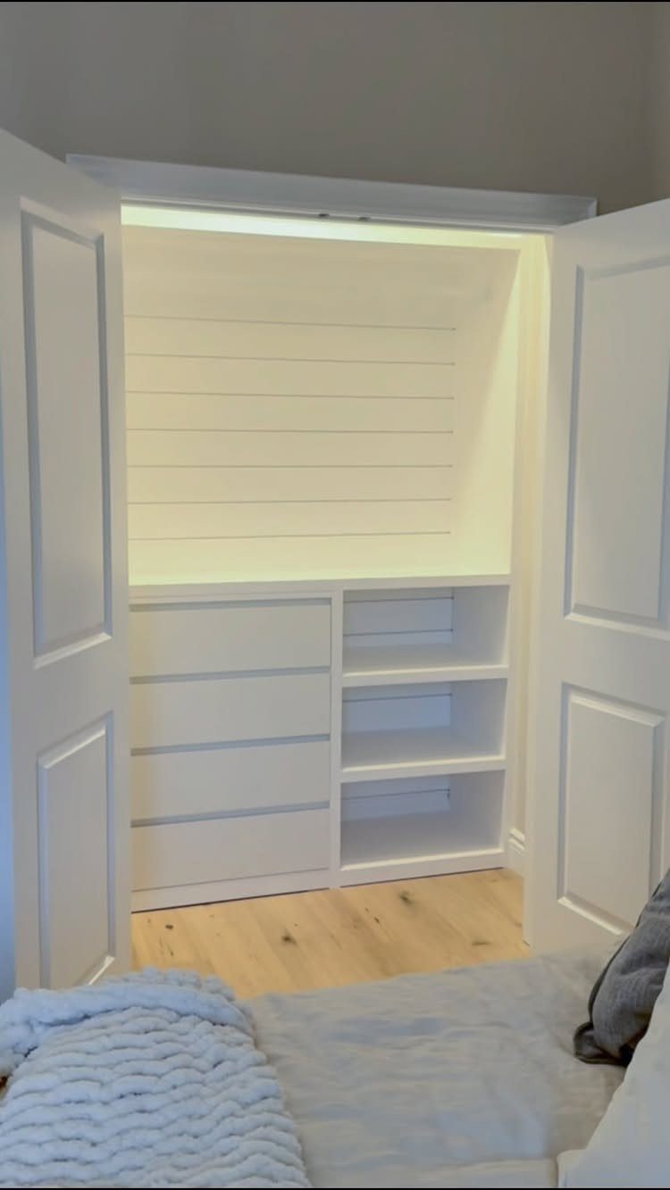 White walk-in closet with shiplap backing, drawers, and open shelving behind paneled doors.
