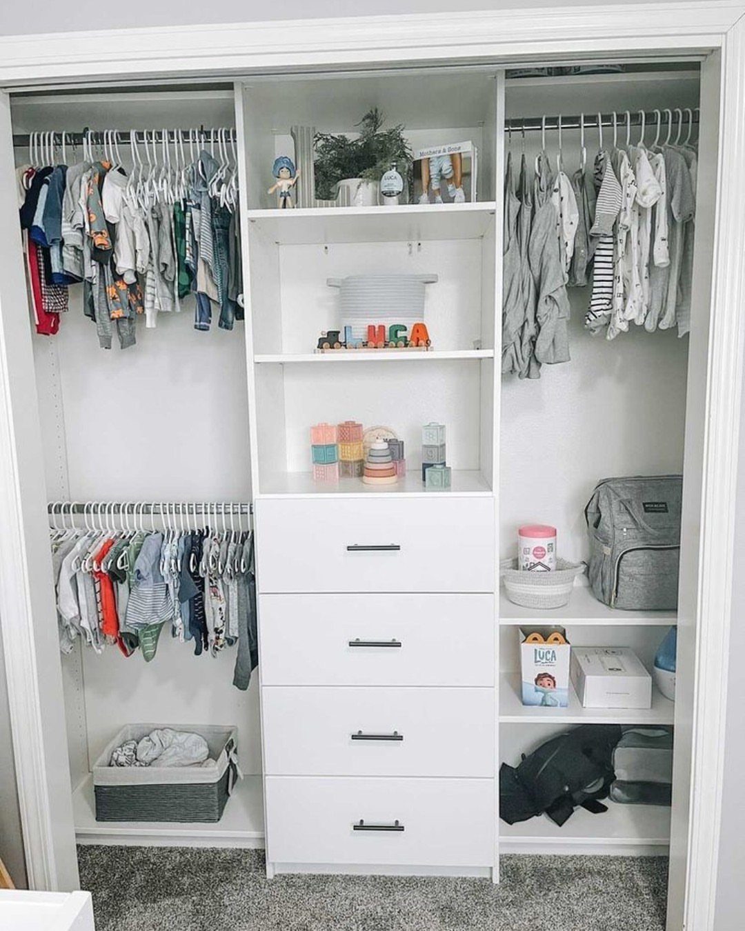 White built-in closet system with custom shelving, drawers, and baby clothes hanging.