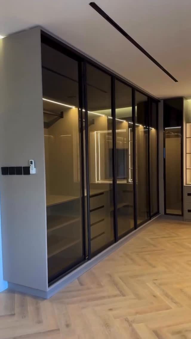 Modern walk-in closet with black-framed glass sliding doors and herringbone wood floors.
