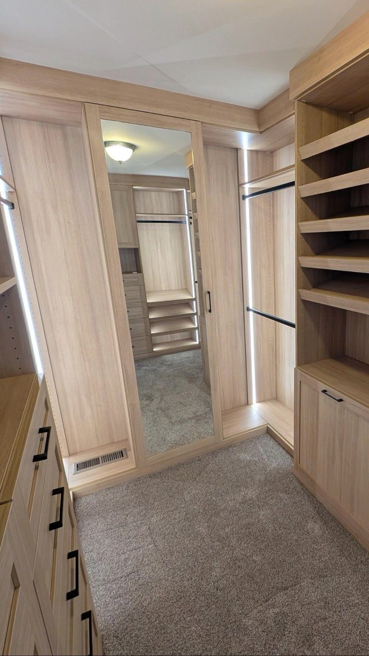 Light wood walk-in closet with a mirrored hinged door and integrated LED lighting.