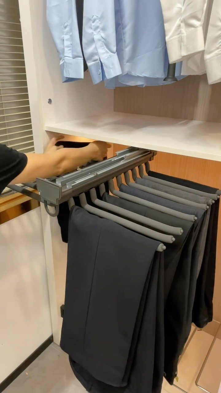 Sliding grey metal trouser rack holding dark pants in a white closet