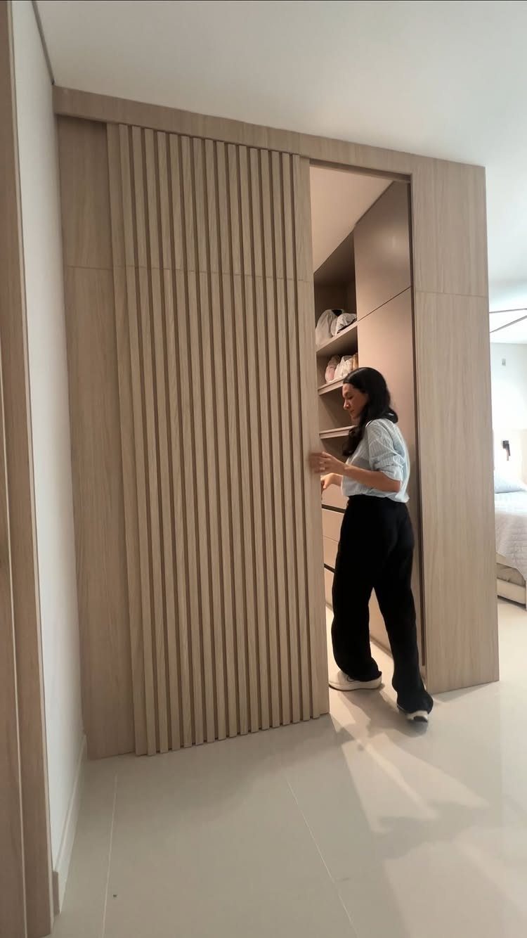 Woman standing next to a light wood walk-in closet with slatted sliding doors.