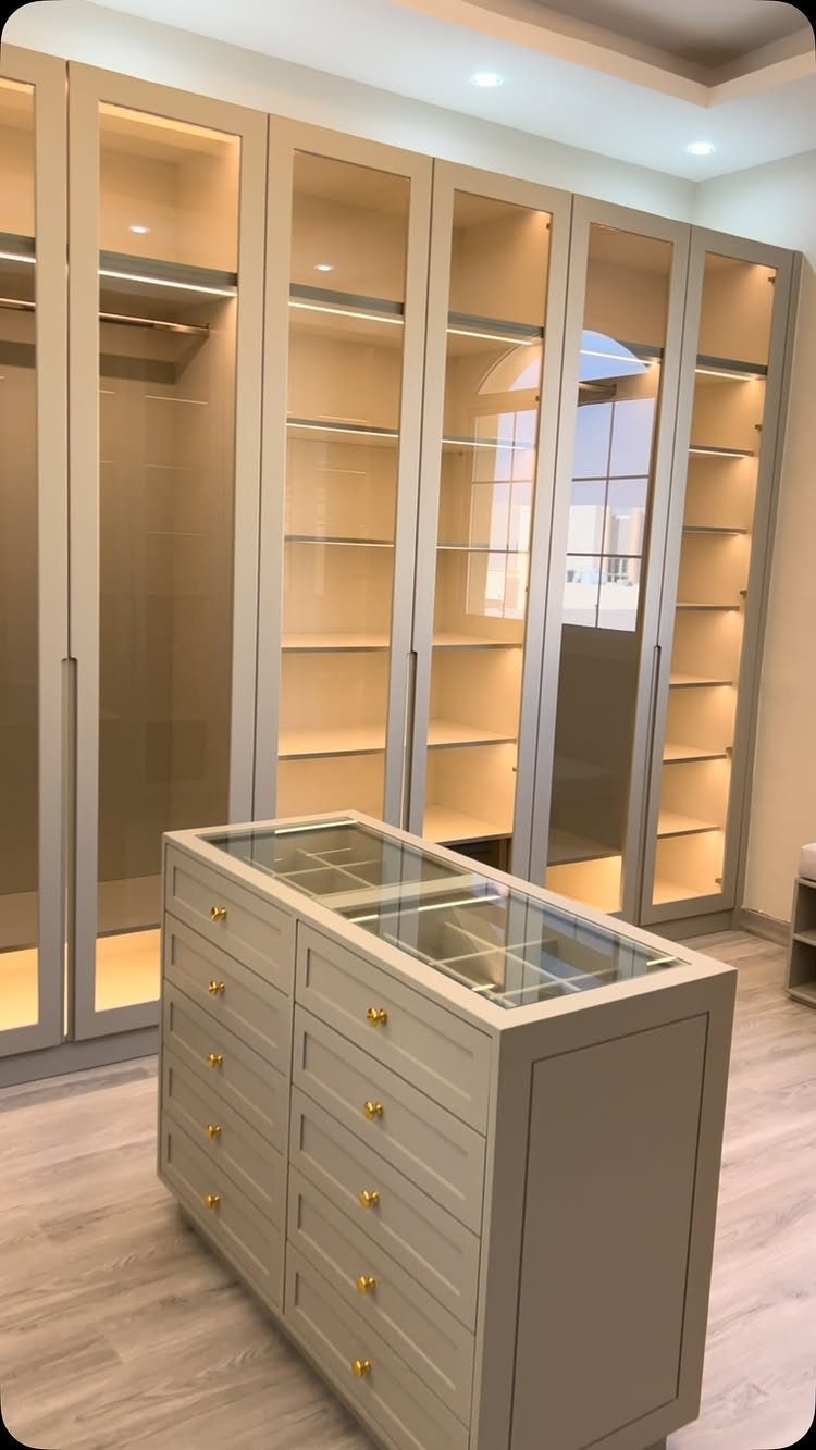 Luxury walk-in closet with beige glass-door cabinets and a central storage island.