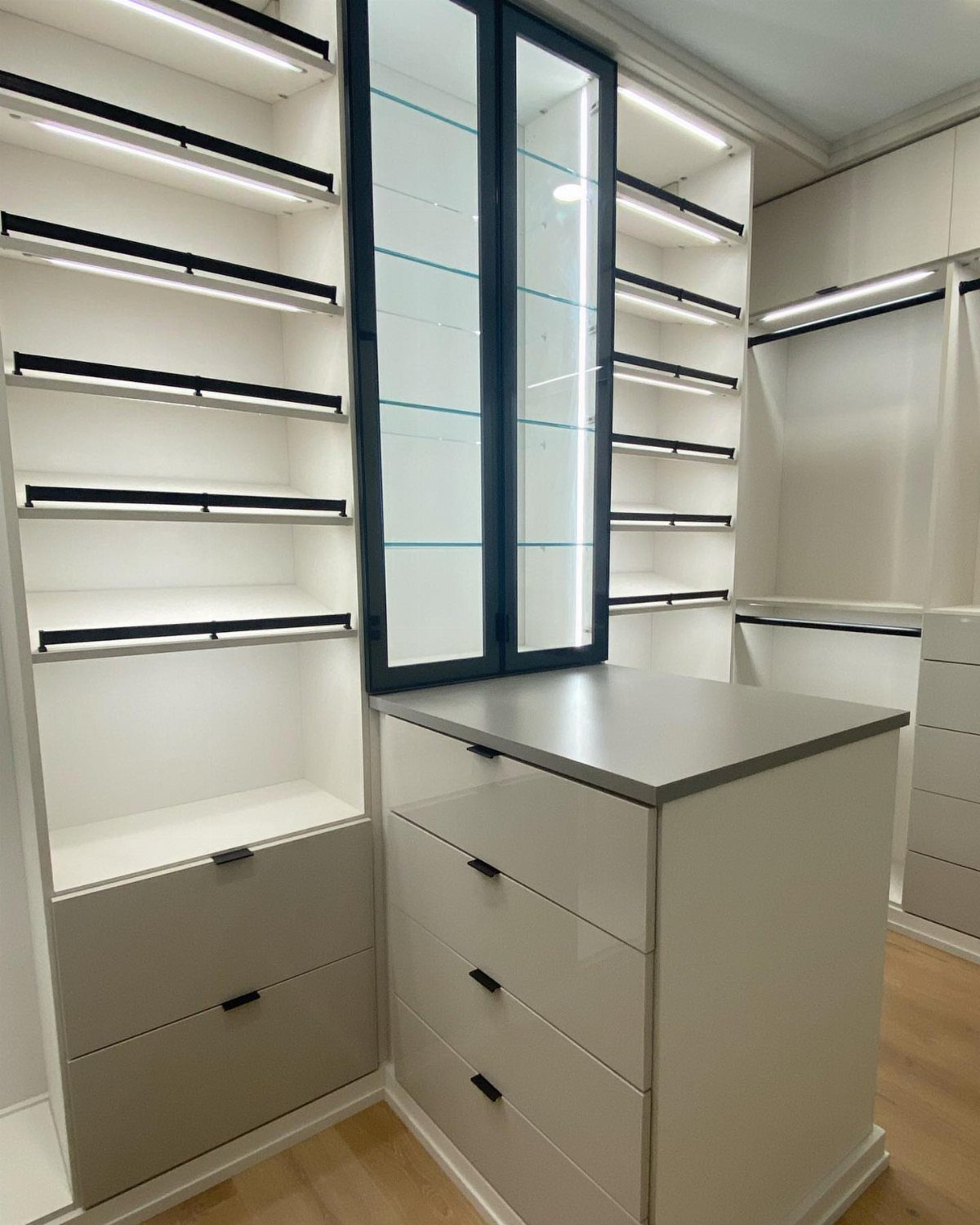 Modern white walk-in closet with a central storage island and illuminated shelving.