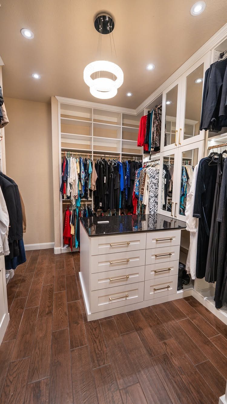 White closet island with black countertop and gold drawers in a walk-in closet.