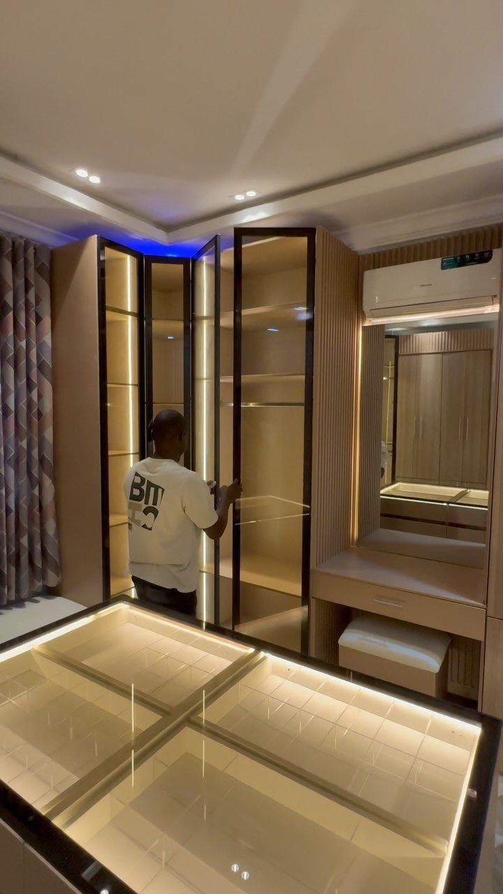 Modern walk-in closet with light wood cabinets and a central illuminated glass island.