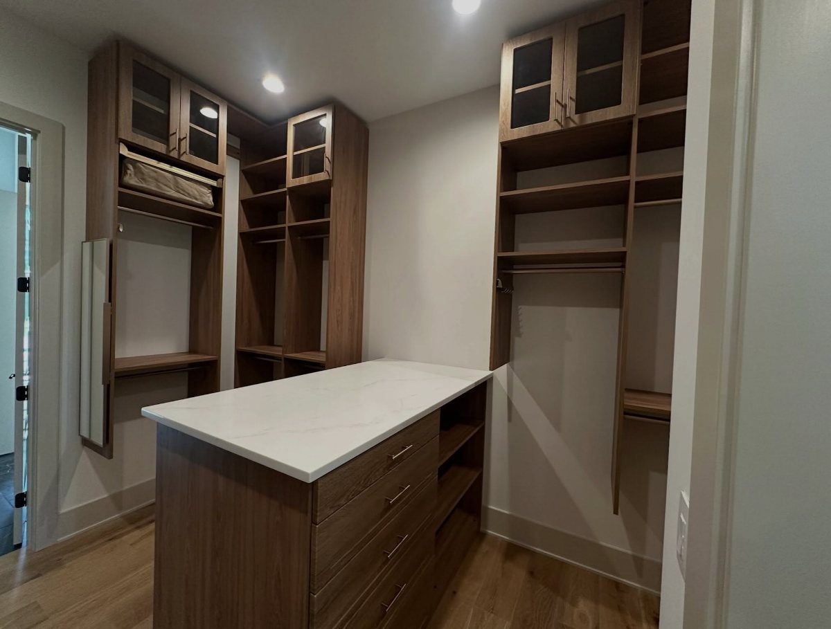 Walk-in closet with brown wooden shelving and a white marble center island.