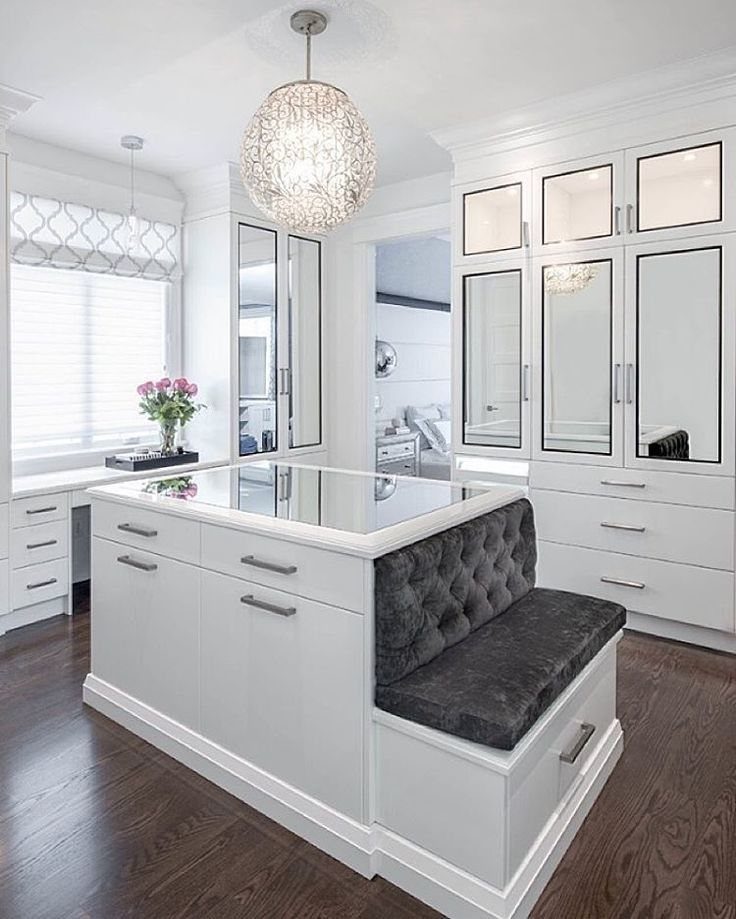 Central island with glass top and grey tufted bench in white walk-in closet