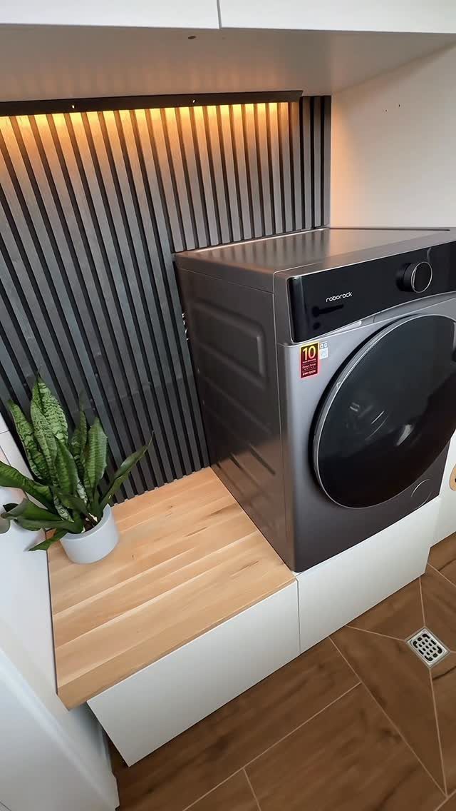 Grey washing machine next to a light wood countertop with a potted plant