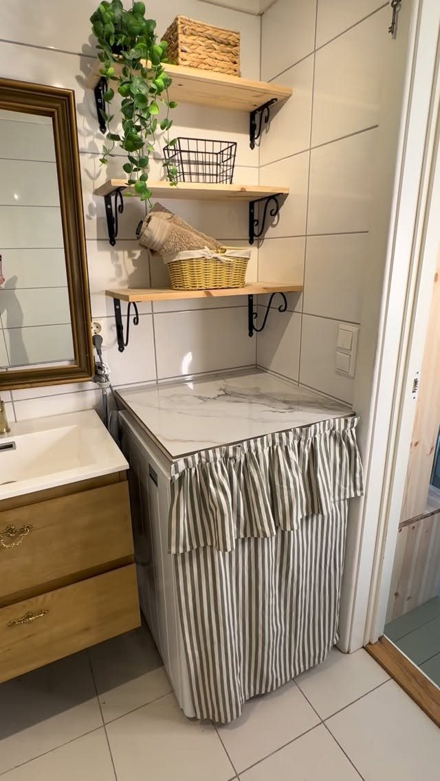 Washing machine hidden by a striped fabric cover under wooden wall shelves.