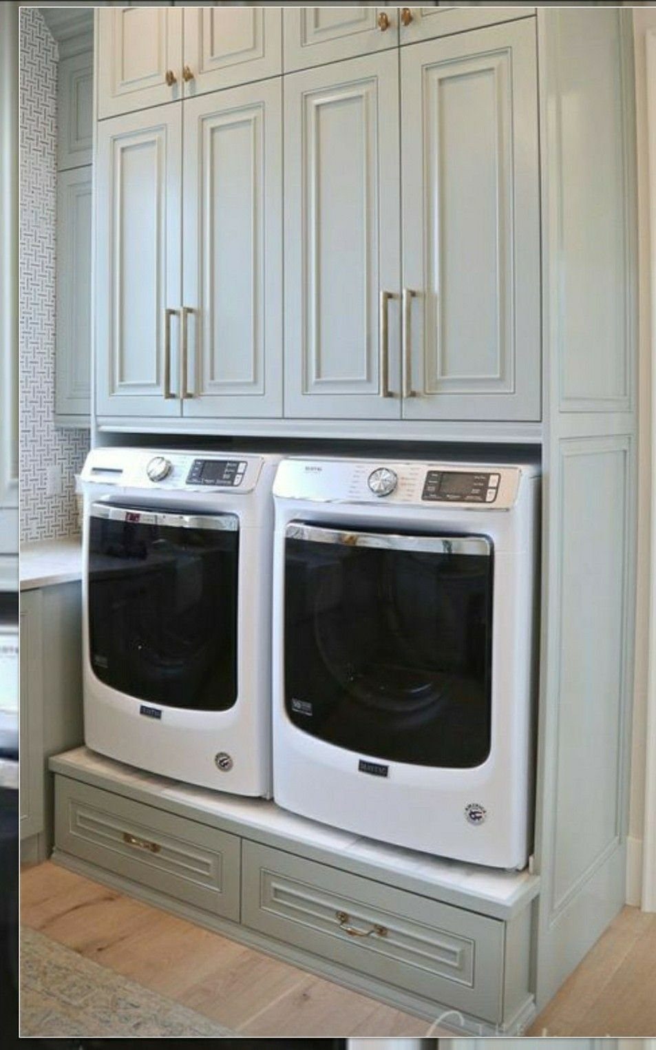 White washer and dryer on a custom grey wooden pedestal with storage drawers.