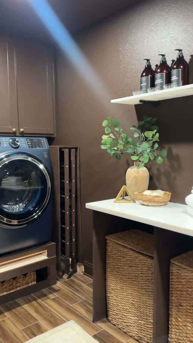 Blue washing machine on a wooden pedestal with a wicker storage basket below.