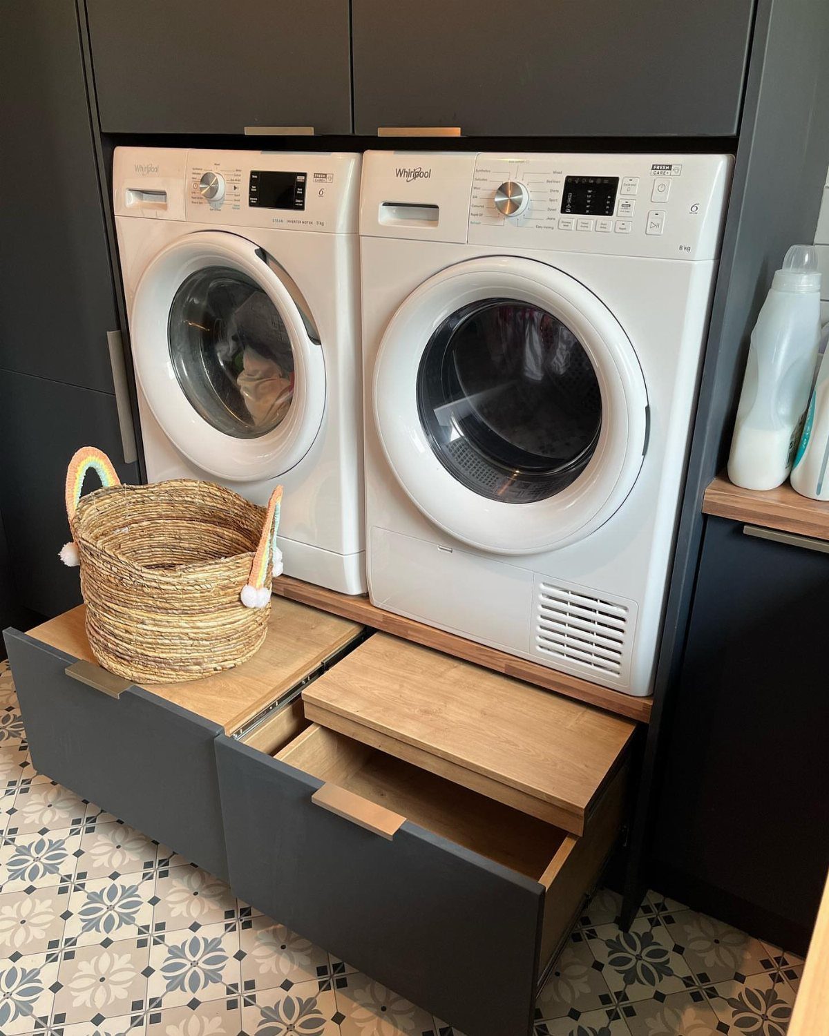White washing machines on a custom wooden pedestal with grey storage drawers.