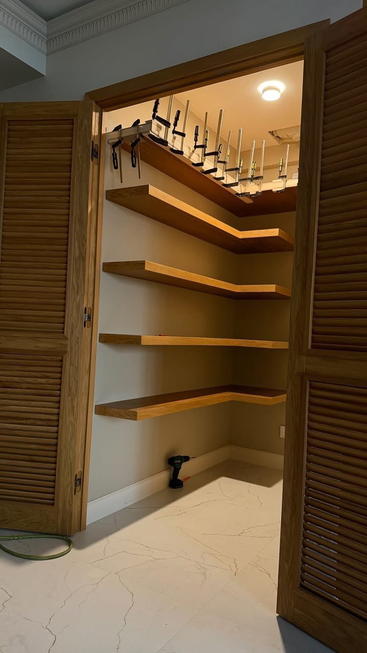 L-shaped light-brown wood shelves installed in a walk-in closet with louvered doors.