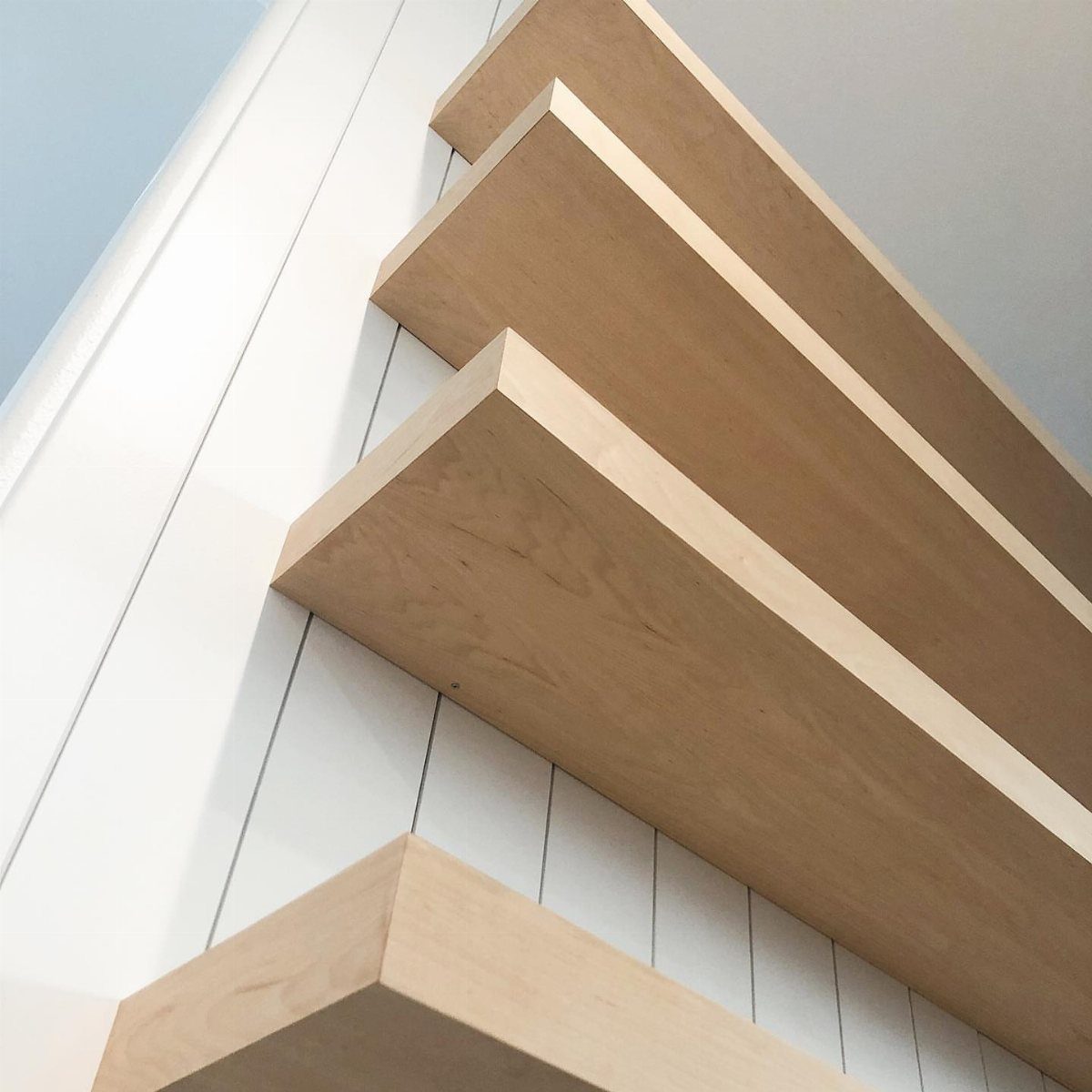 Light wood floating shelves mounted on a white paneled wall in a closet.