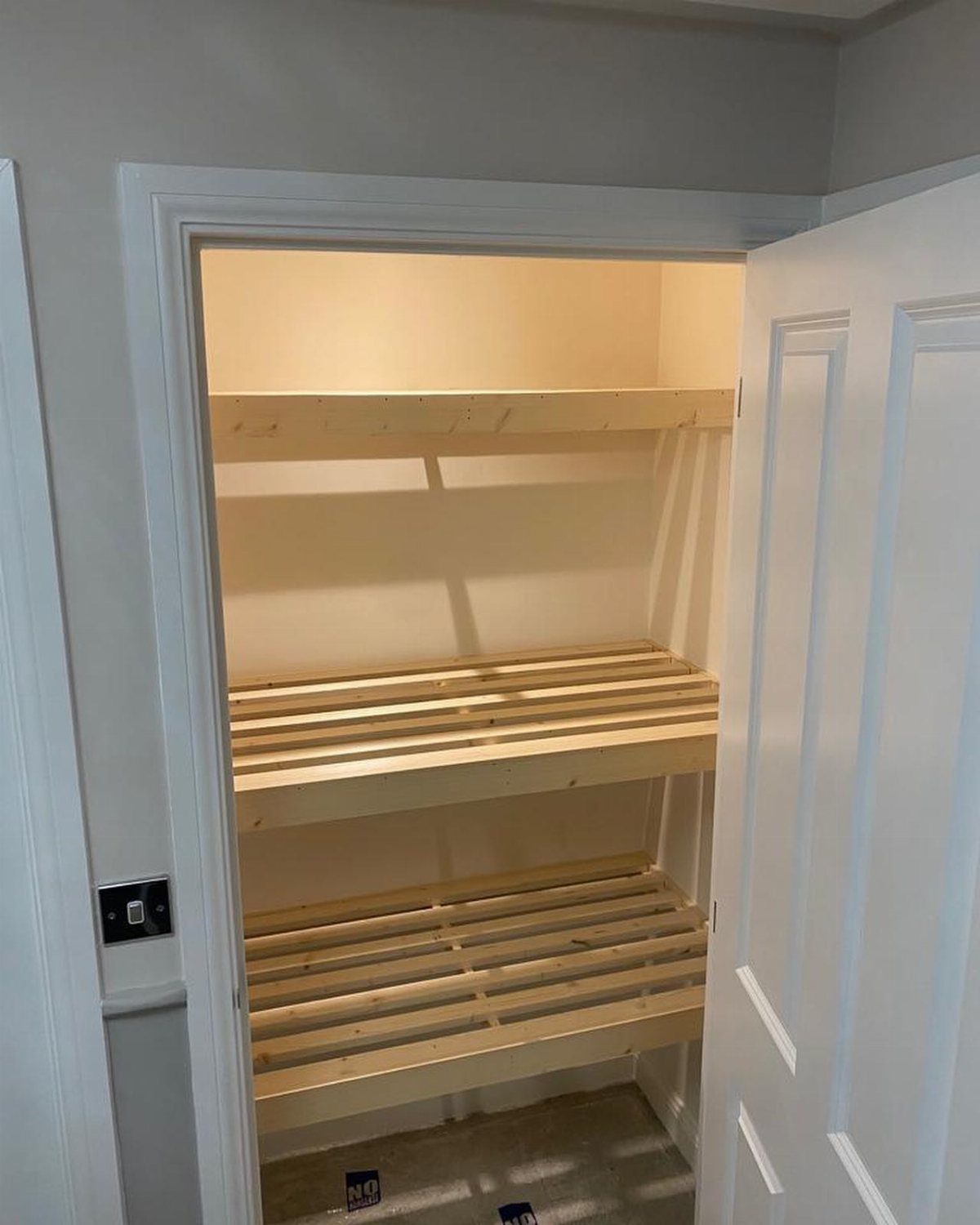Light wood shelves with slatted bottoms inside a white walk-in closet.