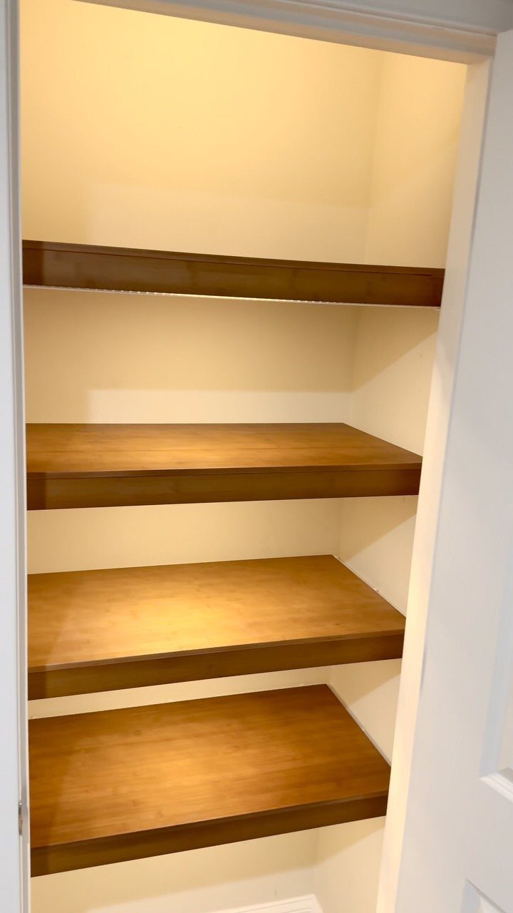 Brown wooden shelves installed inside a white closet with cream walls.