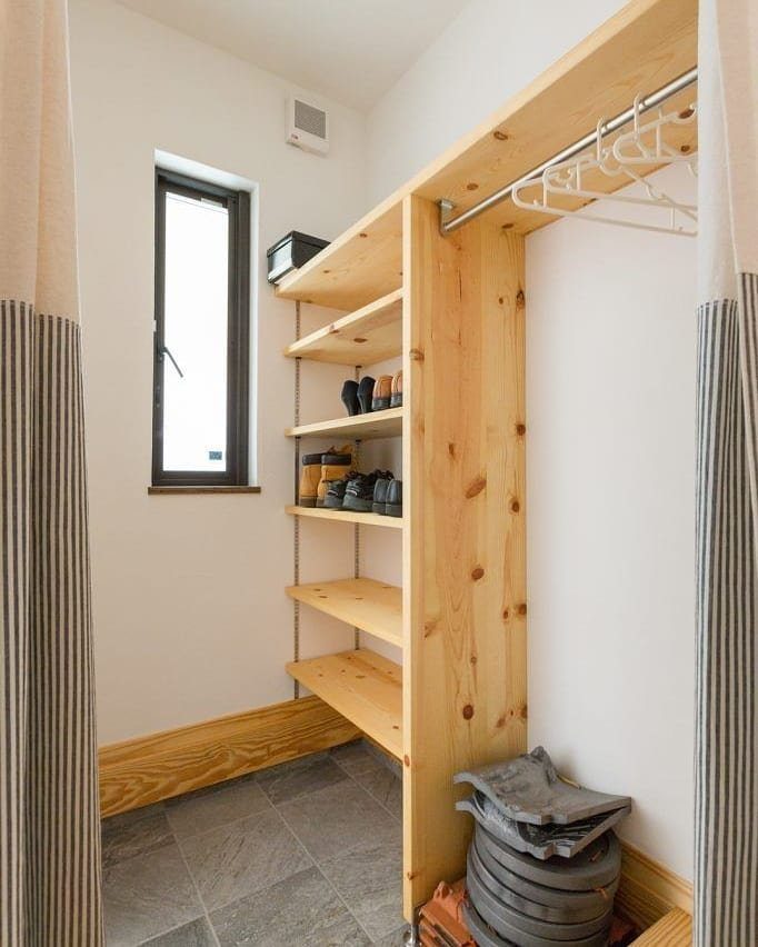 Light wood shelves and hanging rod in a white walk-in closet with tiled floors.